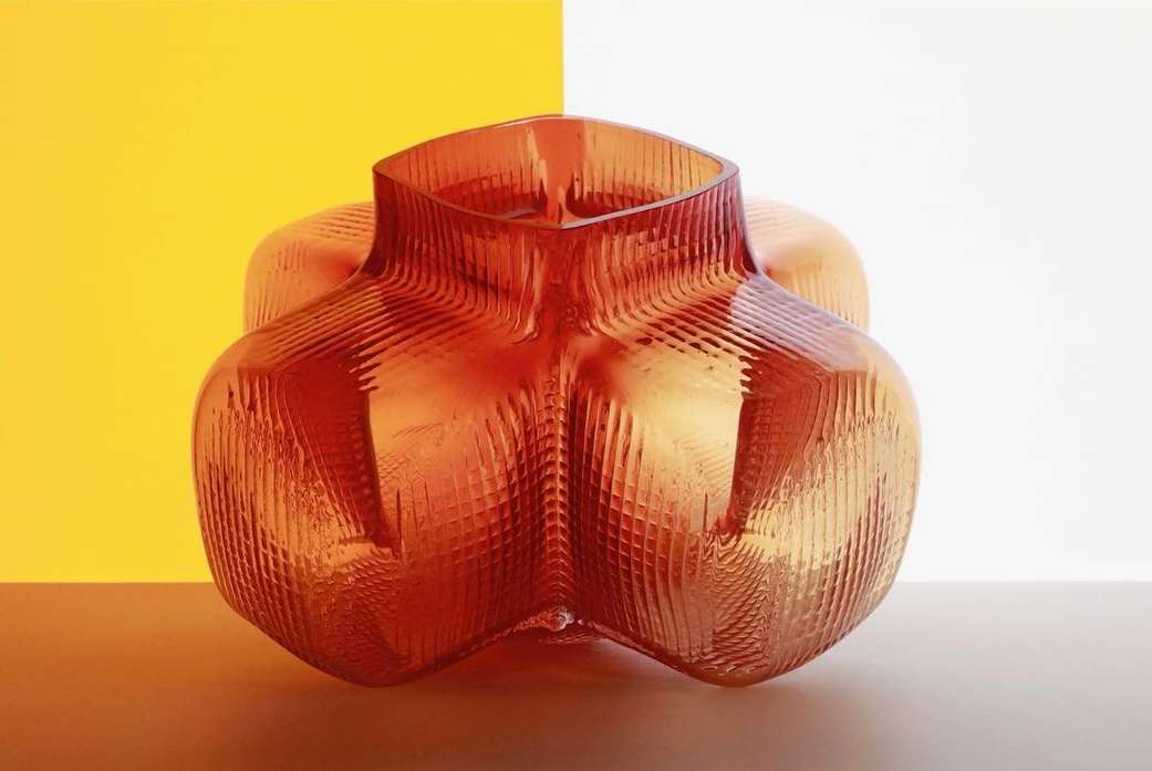 Textured amber-toned glass vase sits on a neutral surface against a split background of yellow and white, showcasing modern design.