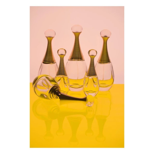 Arrangement of perfume bottles on a yellow surface against a pink backdrop, featuring multiple glass vessels with distinct golden caps.