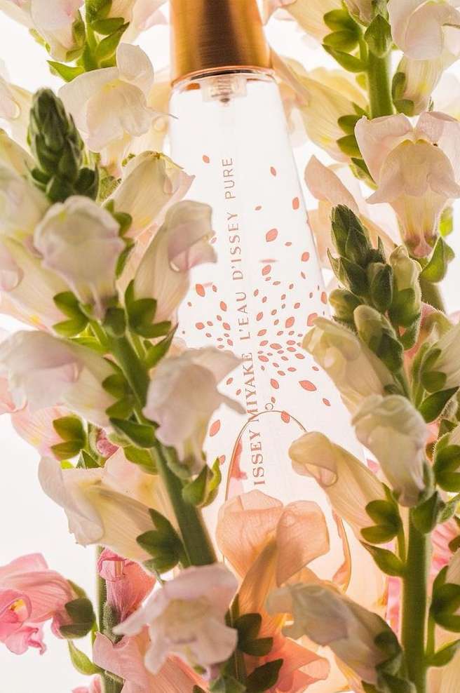 Issey Miyake fragrance bottle is featured in a close-up surrounded by white and pink snapdragon flowers with a bright, soft lighting.