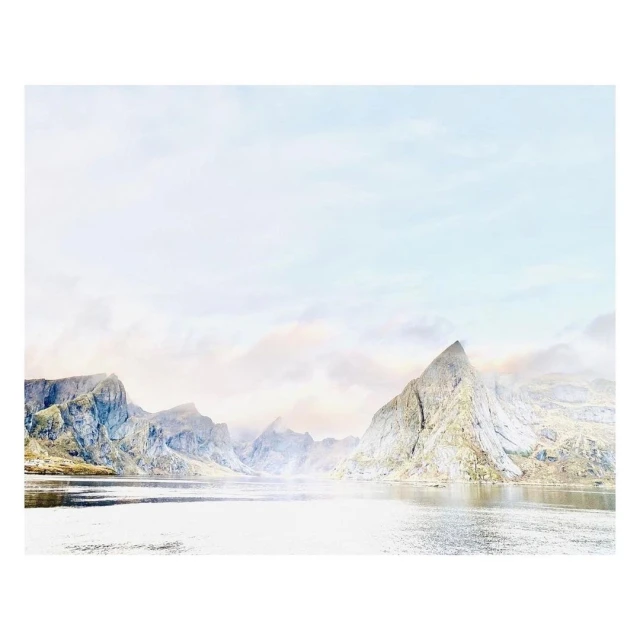 Landscape view of a reflective body of water surrounded by misty, rocky mountains under a light sky, showcasing a serene nature scene.