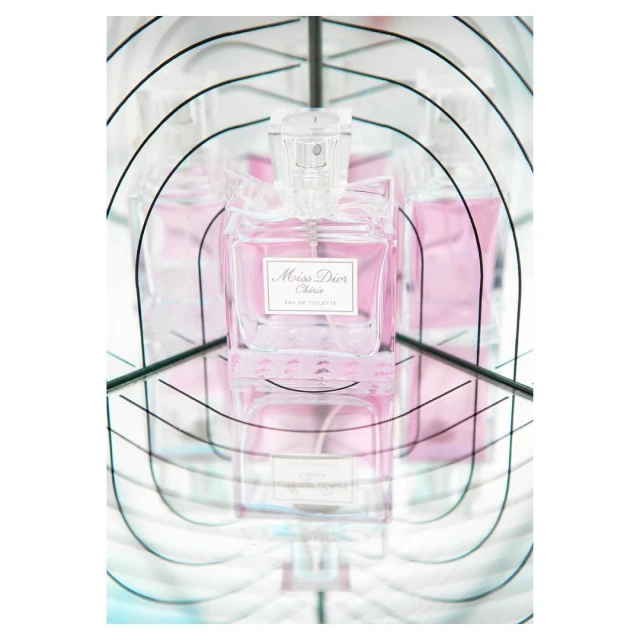 Close-up of a bottle of Miss Dior Cherie Eau de Toilette with a clear cap, set against a mirrored background that creates multiple reflections.
