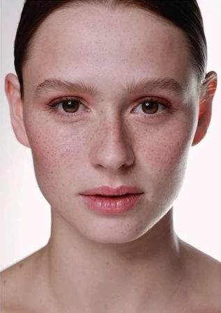 Close-up portrait of a young woman with light freckles and natural makeup against a plain white background