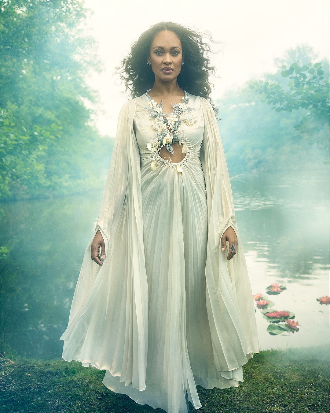 Elegant woman in flowing white dress stands gracefully by a serene lake surrounded by lush green trees and misty air in a fantasy setting.