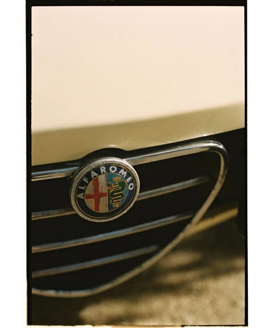 Close-up of an Alfa Romeo car featuring the vehicle's brand emblem on its front grille, with a vintage aesthetic.