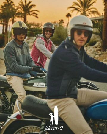 Three adult men riding motorcycles on a road lined with palm trees during a sunny day. They are wearing helmets and sunglasses.