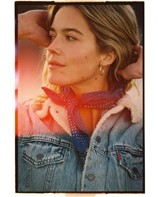 A woman with blonde hair, wearing a denim jacket and a blue bandana, looks off to the side with a soft, natural-light glow.