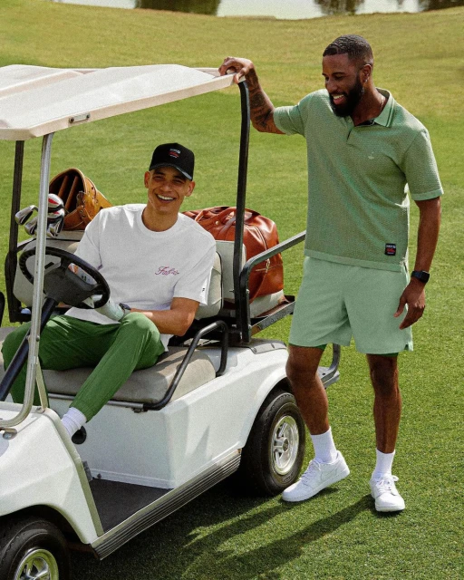 Two adult men on a golf course with a golf cart, wearing sporty casual clothing in light green tones on a sunny day.
