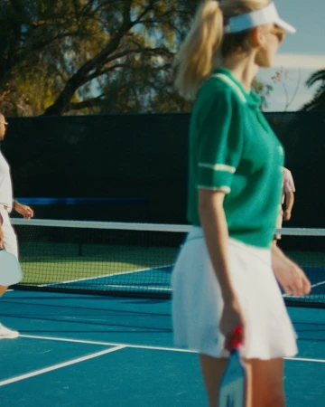 People playing pickleball on an outdoor blue court, wearing athletic clothing and visors, with trees in the background on a sunny day.
