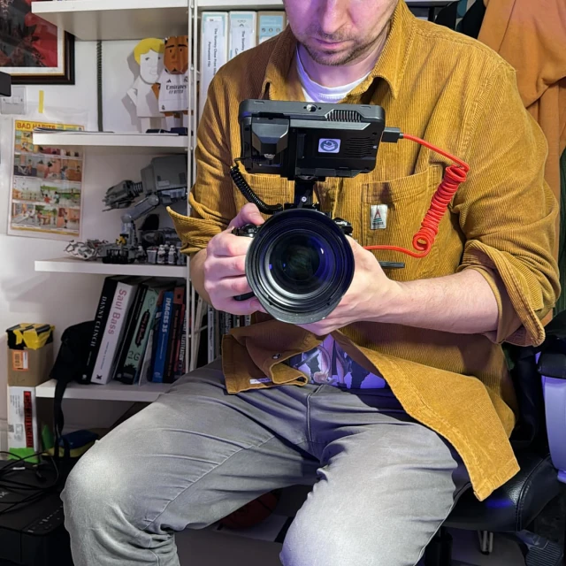 Person holding professional camera with external monitor, set against a background of shelves with books and decorations.