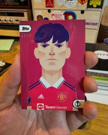 Close-up of a hand holding a sports trading card with a cartoon-style portrait of a soccer player in a Manchester United jersey.