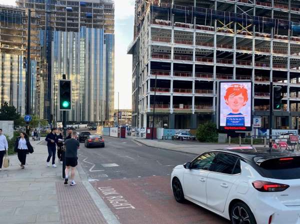 Street scene with pedestrians, a white car, construction, and a digital billboard displaying a portrait in an urban environment.
