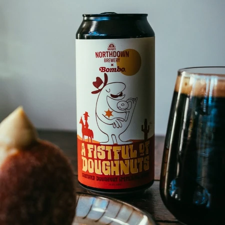 Craft beer can featuring cartoon cowboy character holding donut next to glass of dark beer and two partially visible donuts on a plate.