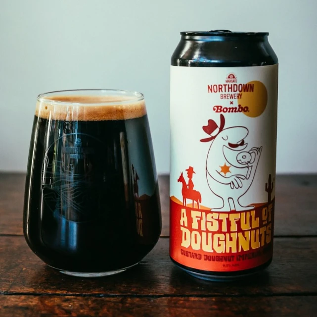 A stout beer in a glass and a can of Northdown Brewery's 'A Fistful of Doughnuts' on a wooden table against a light background.