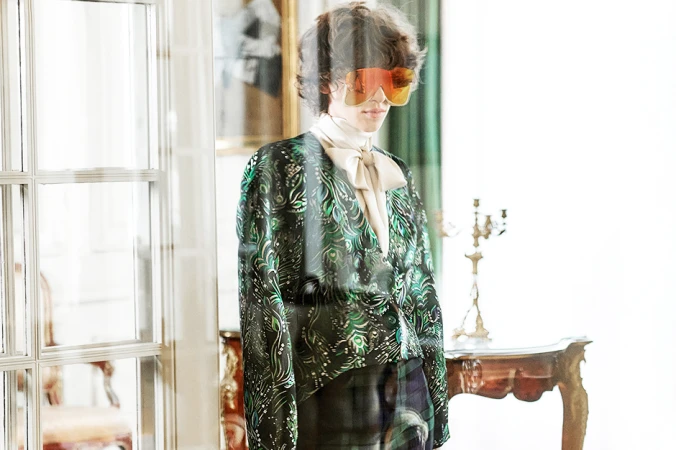 Model wearing oversized orange reflective sunglasses and a green patterned blouse styled by Sandy Karagianni in Athens