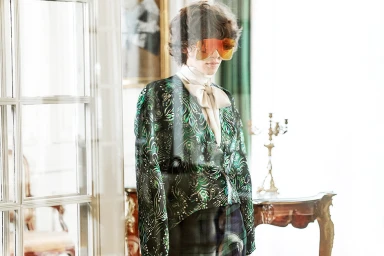 Model wearing oversized orange reflective sunglasses and a green patterned blouse styled by Sandy Karagianni in Athens