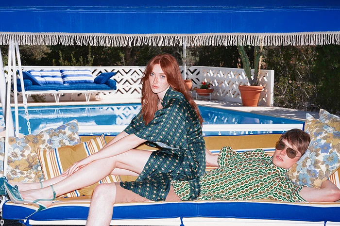 Red-haired woman and man in patterned green matching outfits relaxing on a blue-and-white outdoor poolside swing in Athens styled by Sandy Karagianni
