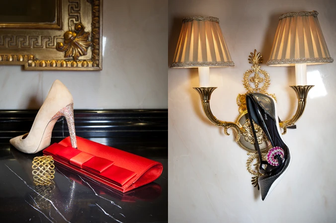 High heel shoe resting on a red clutch next to a gold bracelet on a dark marble surface, with a second shoe hung on a decorative sconce