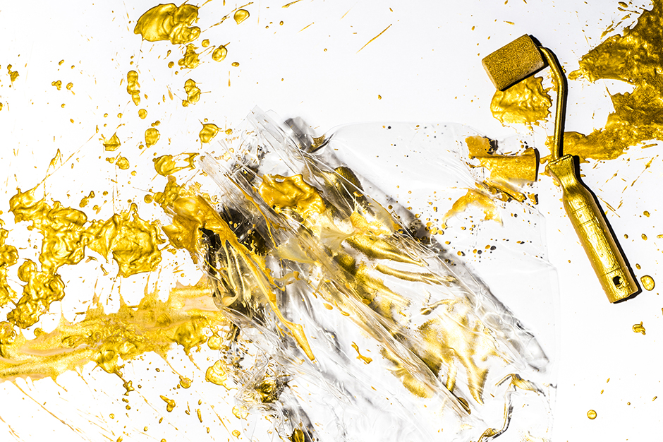 Golden paint splatters and a paint roller over crumpled clear plastic on a white background