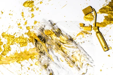 Golden paint splatters and a paint roller over crumpled clear plastic on a white background