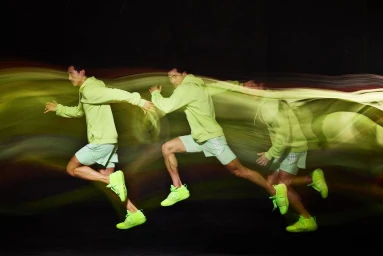 Long exposure photography showing a male runner in neon green hoodie and shorts moving across a dark background.