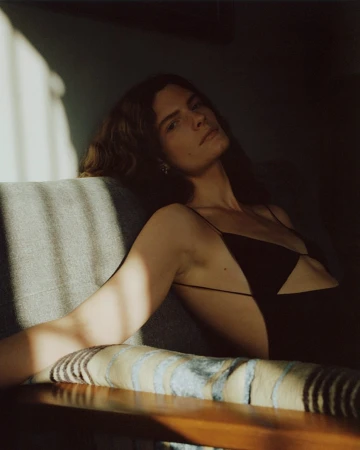 Woman in a black dress reclining on a sofa under warm directional light by photographer Stanislaw Boniecki