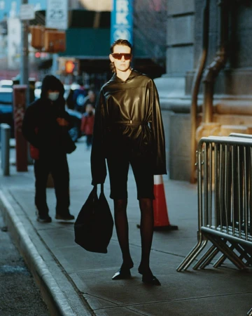 Model wearing dark oversized top and sunglasses holding a black handbag on a New York street by Stanislaw Boniecki