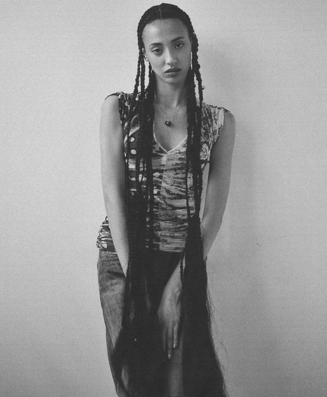 Black and white studio shot of an adult woman with long braided hair, wearing a patterned tank top and denim skirt.