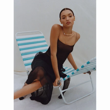 Model wearing a black dress seated in a blue and white striped lounge chair