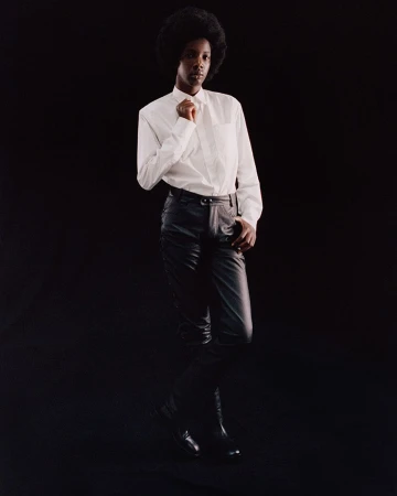 Model with afro wearing a white button-down shirt and black leather pants against a black background