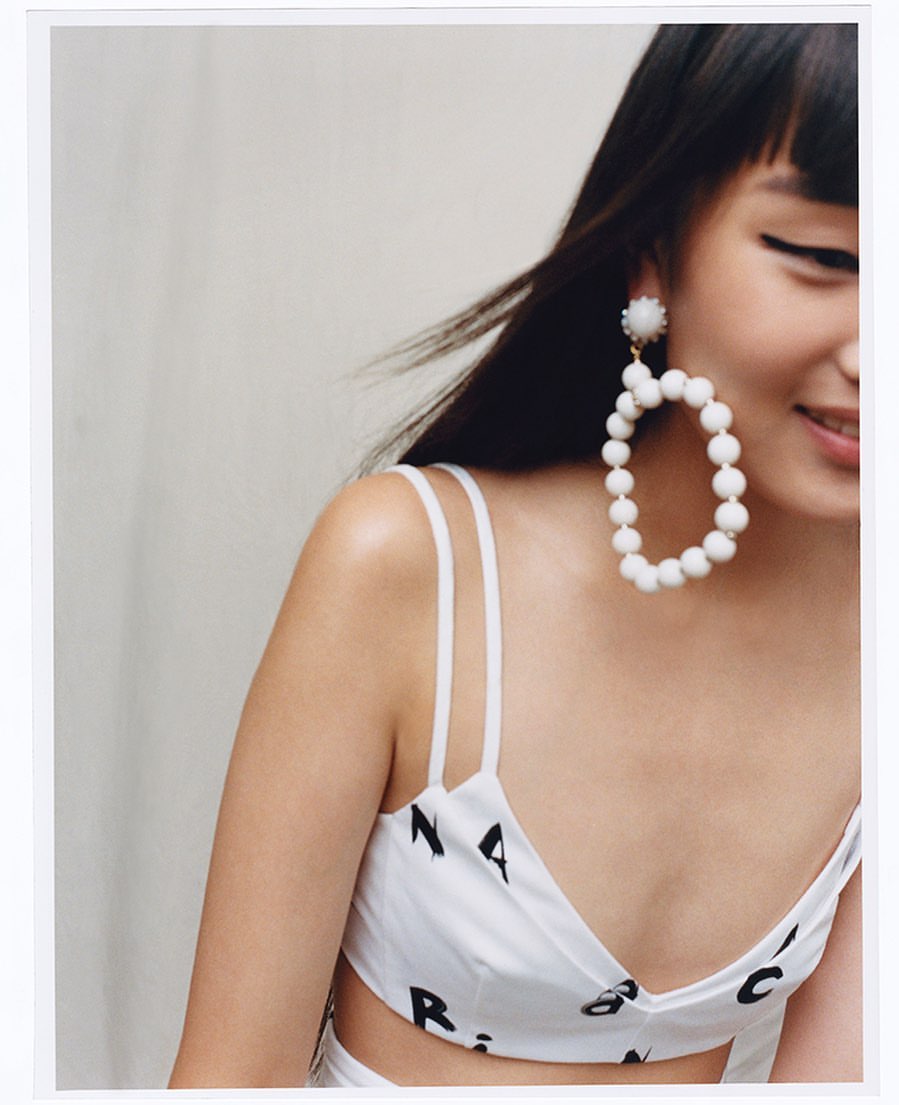 Close-up portrait of a woman wearing large white beaded hoop earrings and a printed white top, shot by Stanislaw Boniecki.