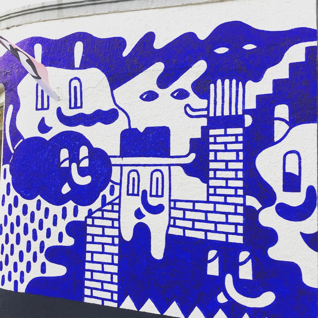 Illustration of cartoon-like figures with building elements, rendered in bright blue and white on an exterior wall surface.