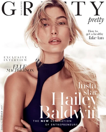 Magazine cover featuring a blonde female model with fair skin, wearing a black swimsuit, and posing against a soft gradient background.