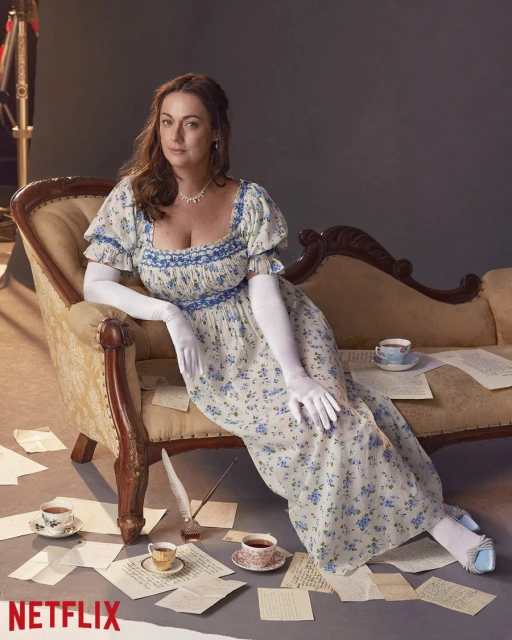 Woman in floral dress sitting on vintage chaise lounge with scattered papers and tea cups in studio setting. Netflix logo visible.
