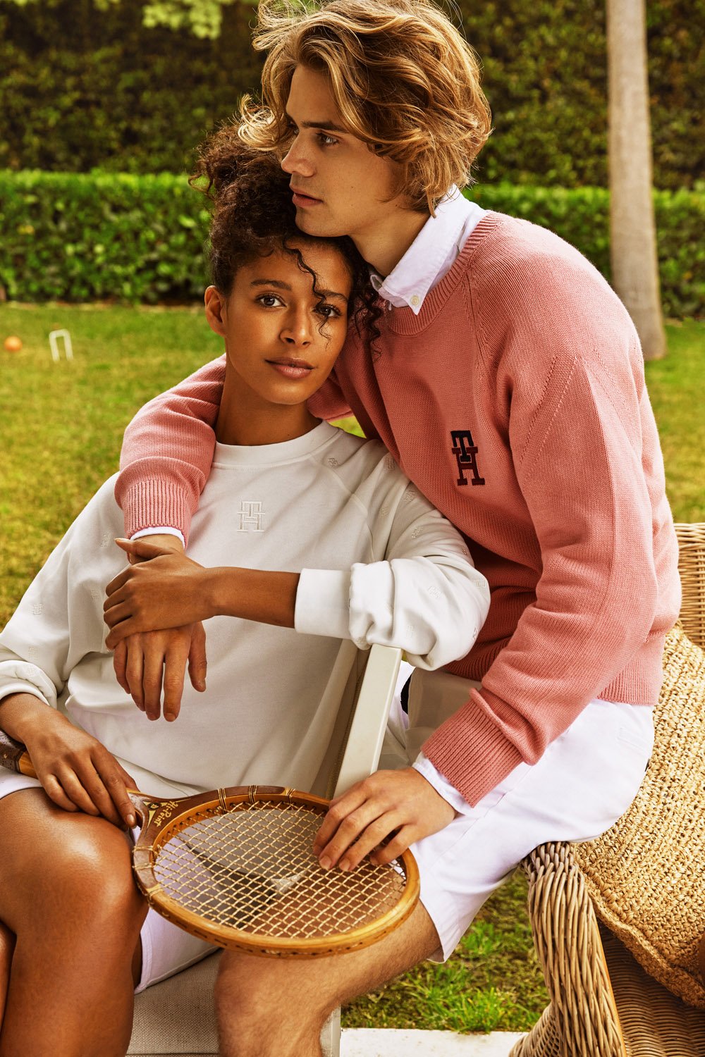An embrace between a woman with an Afro and a man with blonde hair in a sunny outdoor setting, both in casual sweaters.