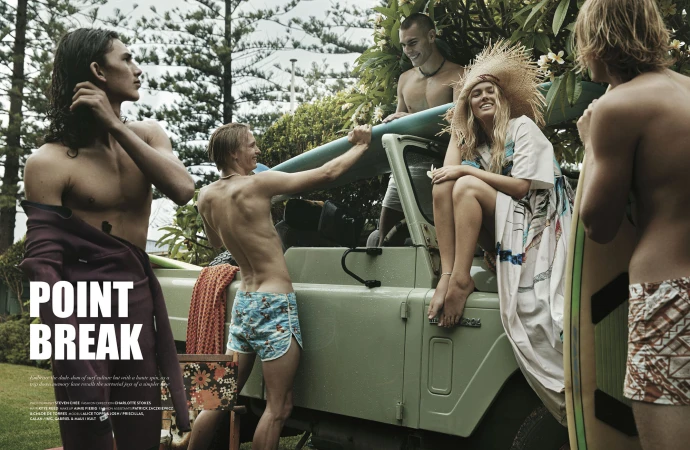Group of young adults with surfboards alongside an olive green off-road vehicle, surrounded by lush foliage in a tropical setting.