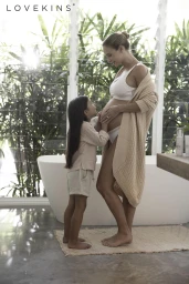 Pregnant woman standing in a bright bathroom wearing a knit cardigan and white top, with a young child touching her belly.