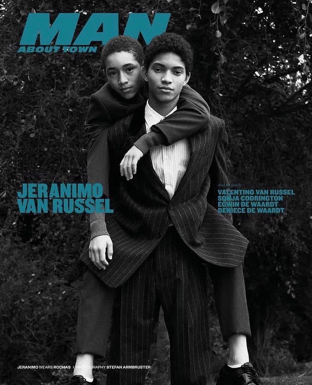 Magazine cover featuring two young men: one giving the other a piggyback ride, both wearing suits against a dark foliage background.