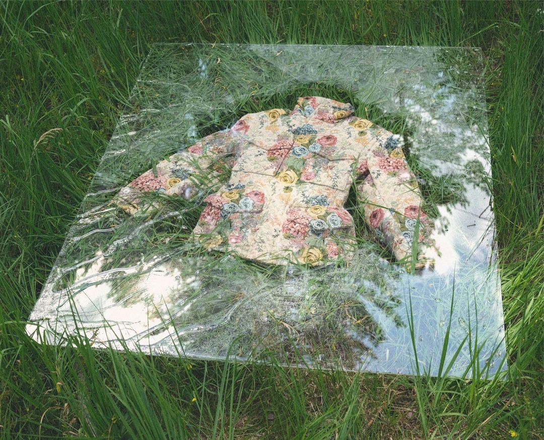 Floral jacket is displayed on a mirror surrounded by green grass in an outdoor setting; spring day, natural lighting.