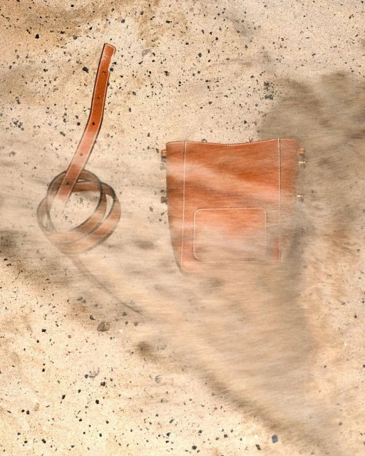 Overhead shot of a brown leather handbag and matching belt on a speckled, sandy-toned surface, evoking fashion and accessory concepts.
