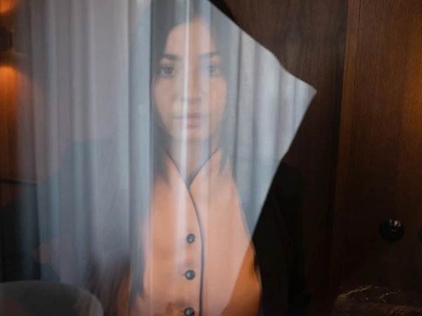Portrait of a woman viewed through sheer vertical blinds and a tilted transparent plastic sheet in New York