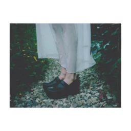 Close-up of black platform shoes on a pebble path framed by green foliage, photographed by Stefan Armbruster.