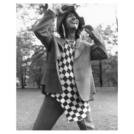 Smiling man in a checkerboard sweater and wide hat posing outdoors in a park by Stefan Heinrichs