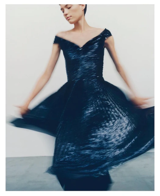 Fashion shot of a woman in motion, wearing an off-the-shoulder blue dress against a white background, promoting clothing and style.