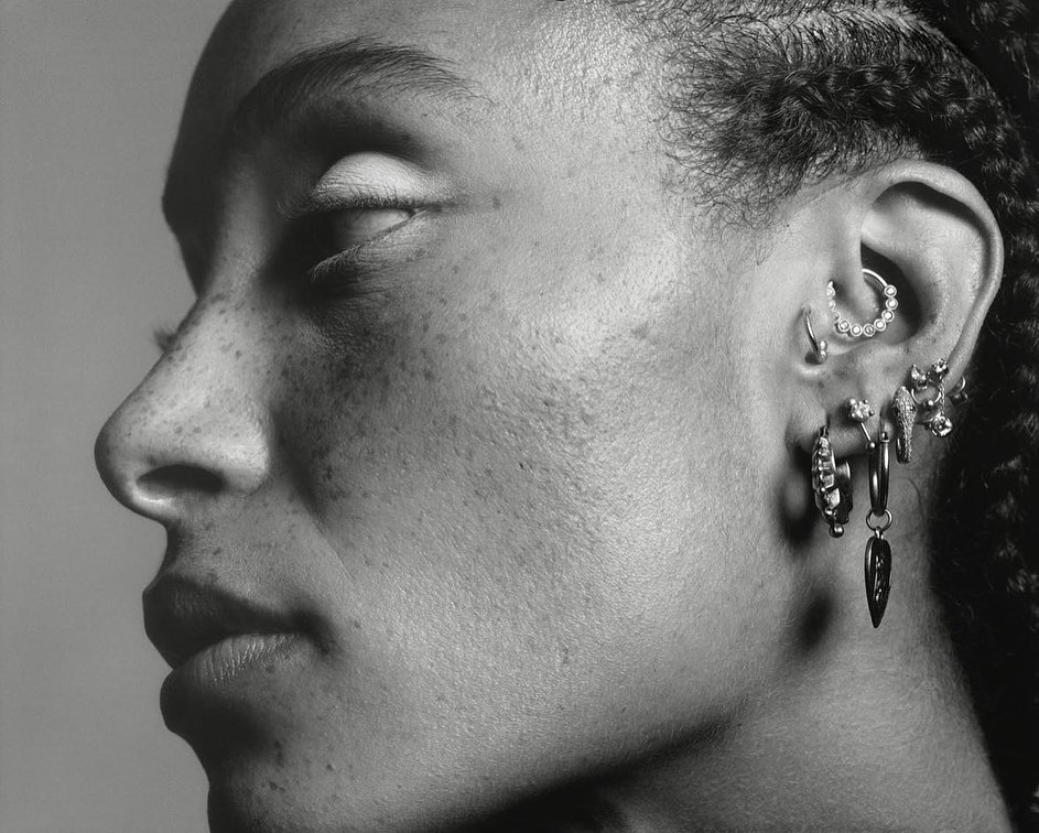 Close-up profile of a black woman wearing multiple silver earrings and facial piercings captured by Stefan Heinrichs