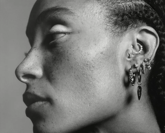 Close-up profile of a black woman wearing multiple silver earrings and facial piercings captured by Stefan Heinrichs