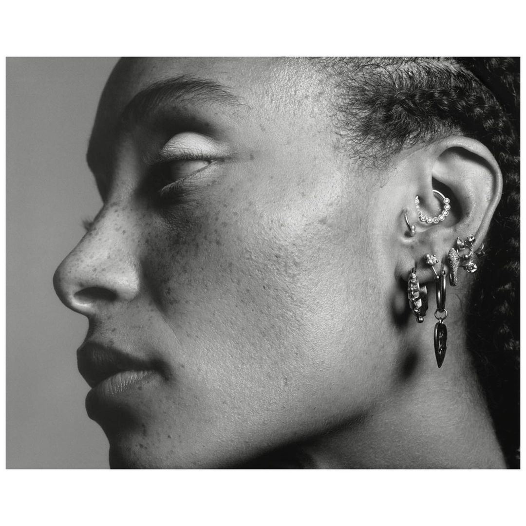 Monochrome close-up profile portrait of a woman showing detailed ear piercings against a neutral background