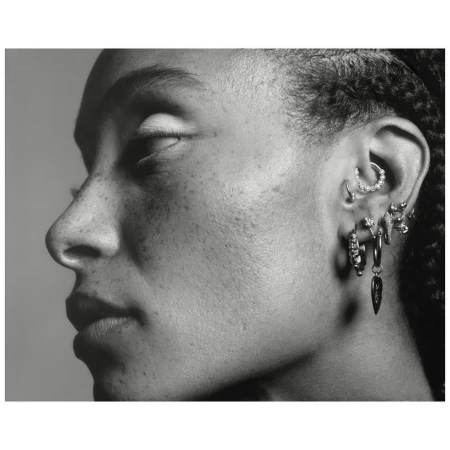 Monochrome close-up profile portrait of a woman showing detailed ear piercings against a neutral background