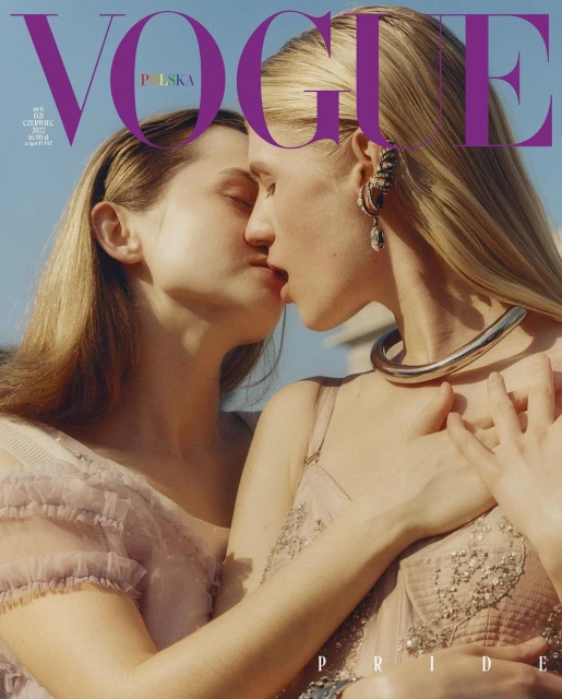Two women embrace in a fashion magazine cover shoot, wearing embellished dresses and statement jewelry, set against a bright outdoor background.