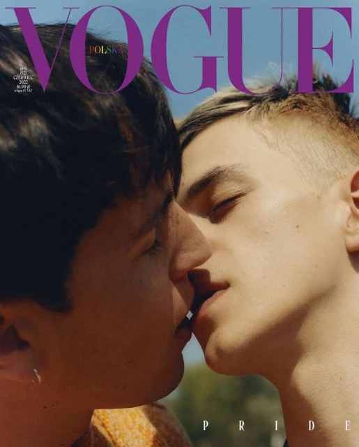 Vogue Polska magazine cover featuring two adult males in a close-up shot, embracing and kissing against a bright blue sky and blurred outdoor background.