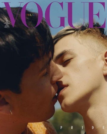Vogue Polska magazine cover featuring two adult males in a close-up shot, embracing and kissing against a bright blue sky and blurred outdoor background.